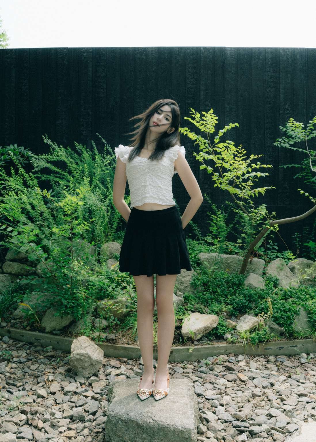 Maram standing in a garden in a white top and black pleated skirt