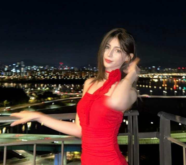 Maram in a red dress on a night balcony, hand raised
