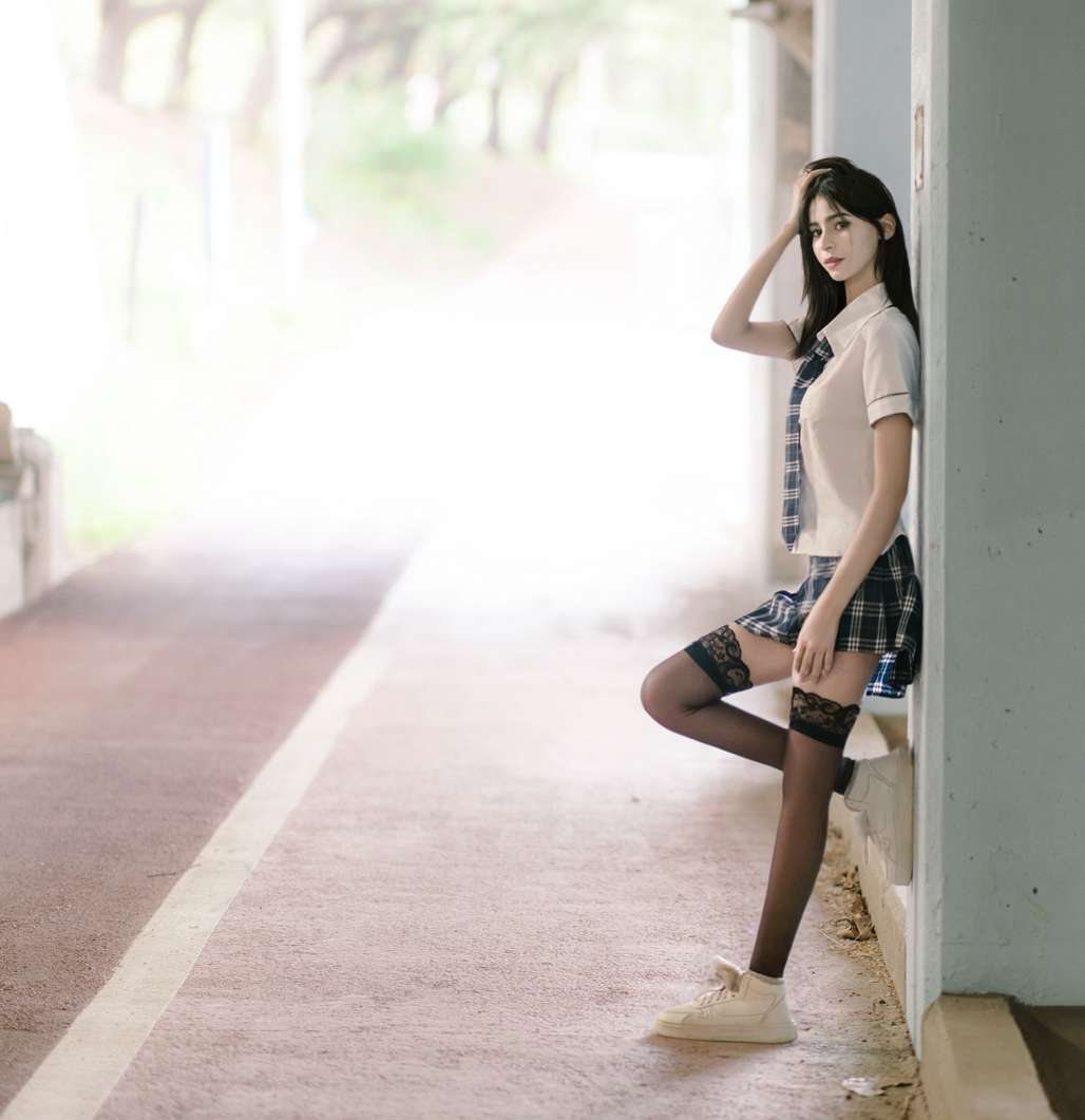 Maram in a school-style uniform leaning on a pillar
