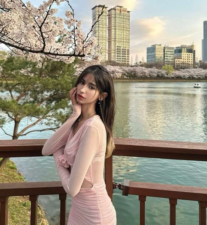 Maram by a lakeside railing with city towers behind
