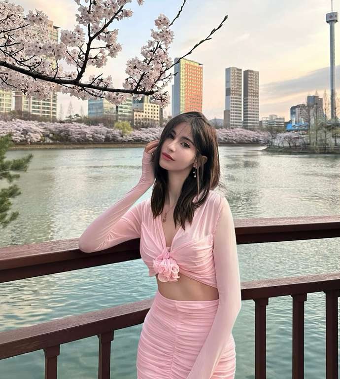Maram touching her hair beside a blossom-lined lake