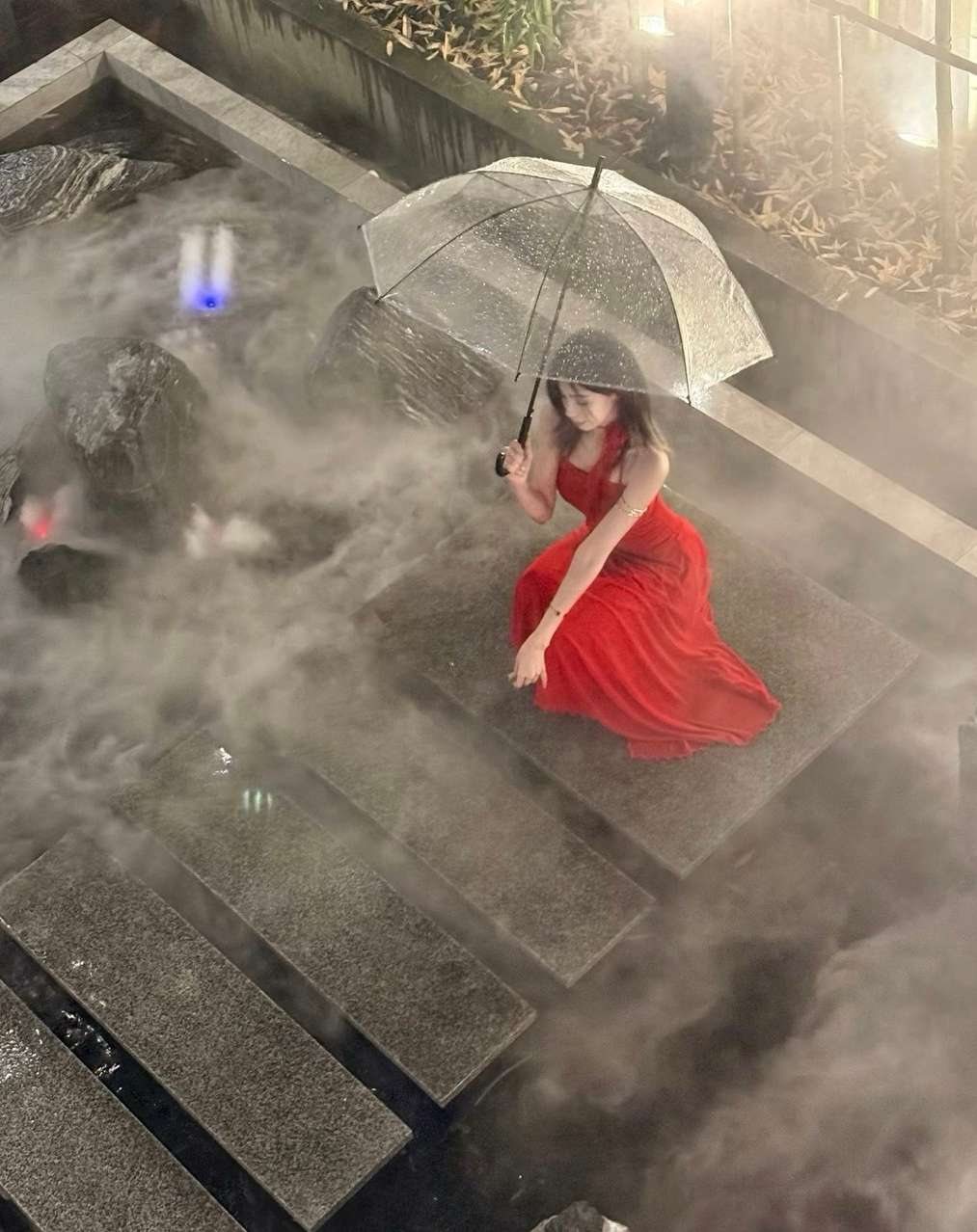 Maram in red under a clear umbrella on misty steps