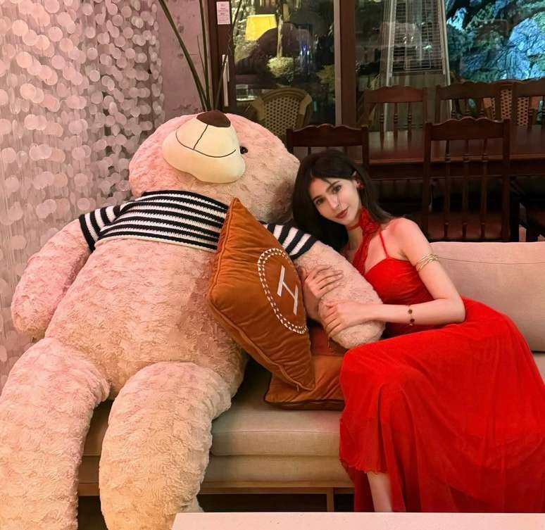 Maram in a red dress leaning on a large teddy bear