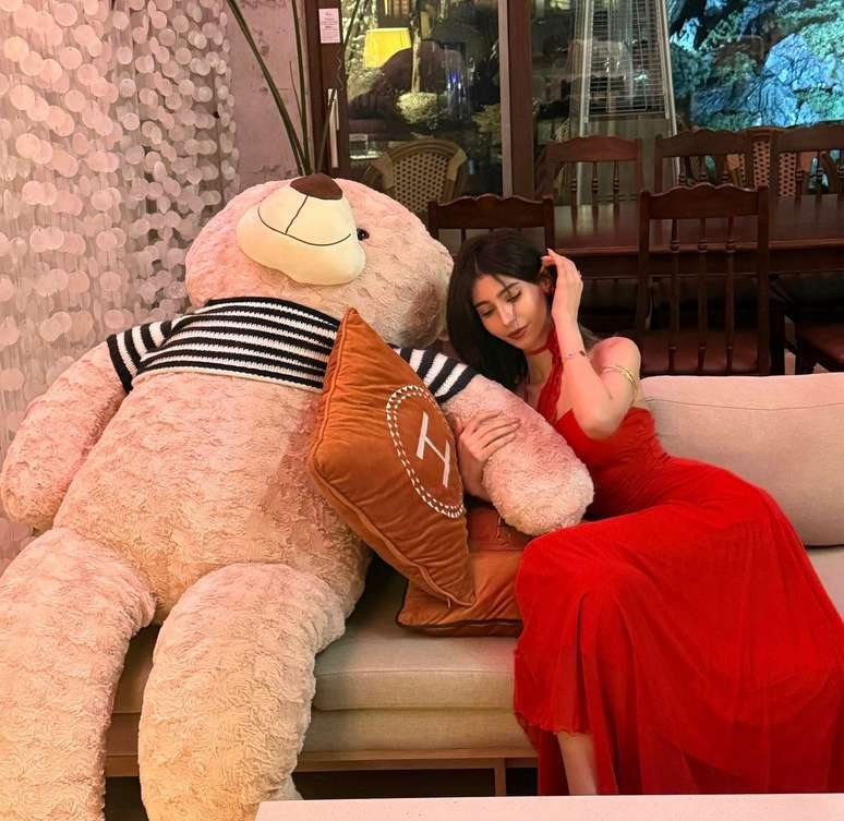 Maram in a red dress resting beside a large teddy bear