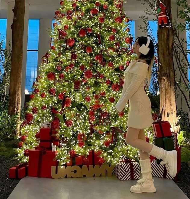 Maram in a cream knit dress and earmuffs by a decorated tree