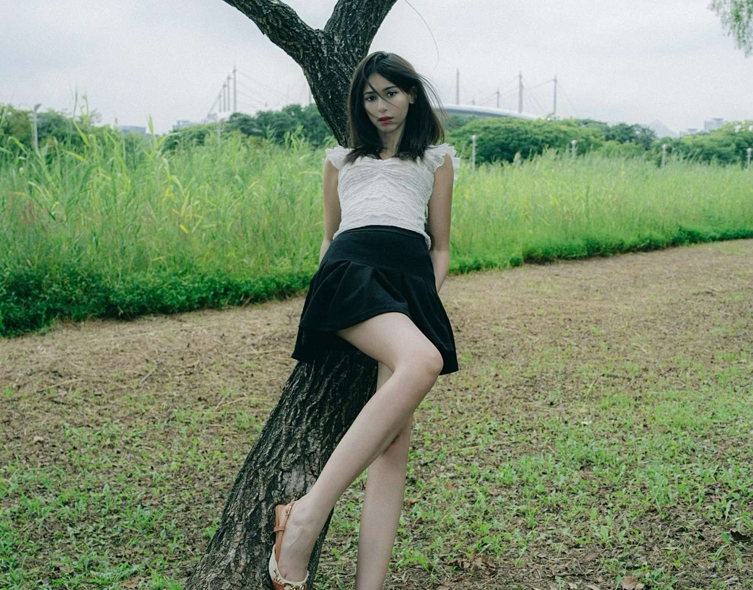 Maram leaning against a tree beside a grass field
